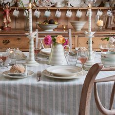 a dining room table with plates, cups and vases filled with flowers on it