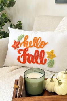 a pillow with the words hello fall on it next to a glass of milk and pumpkins