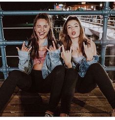 two young women sitting on a bench making the peace sign with their hands and smiling