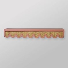 a pink and gold shelf with scalloped edges on a white wall behind it