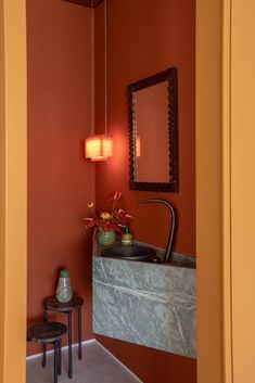 a bathroom with red walls and a marble sink in the corner next to two stools