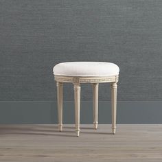 a white bench with a cushion on it in front of a gray wall and wooden floor