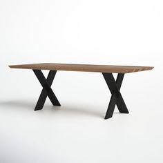 a wooden table sitting on top of a white floor next to a black metal cross leg