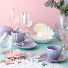 a table topped with purple cups and saucers next to vases filled with flowers