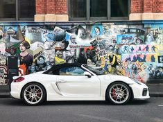 a white sports car parked in front of a graffiti covered wall