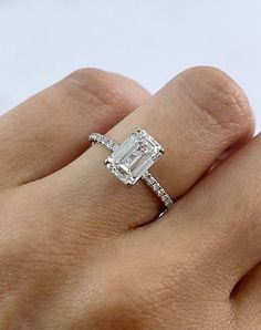 a woman's hand with a diamond ring on top of her finger and an emerald stone in the middle