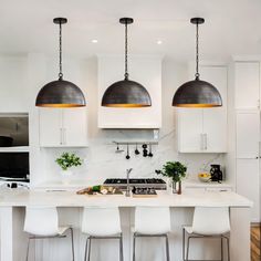 three pendant lights hang over a kitchen island with white chairs and marble countertops in front of an oven