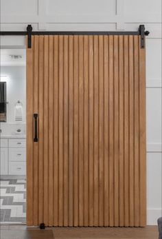 an open sliding door with wooden slats on the side and black hardware, in front of a white kitchen