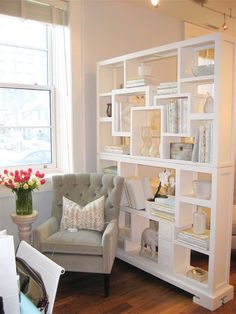 a living room filled with furniture next to a window and a chair in front of a book shelf