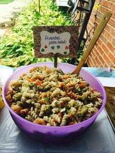 a purple bowl filled with pasta and veggies on top of a table next to a sign