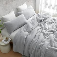 an unmade bed with white sheets and pillows on top of it next to a potted plant