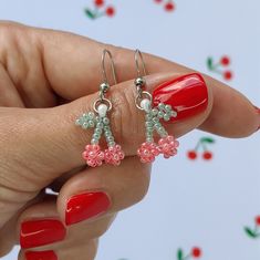 a woman's hand holding two pairs of pink and green beaded flower earrings