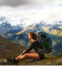 a woman sitting on top of a mountain with a backpack