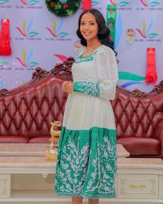 a woman standing in front of a couch wearing a green and white dress with flowers on it