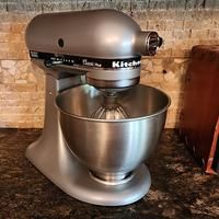 a silver mixer sitting on top of a counter next to a wooden box and brick wall