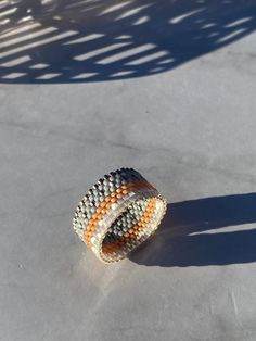 an orange and white beaded bracelet sitting on top of a cement floor next to a person's shadow