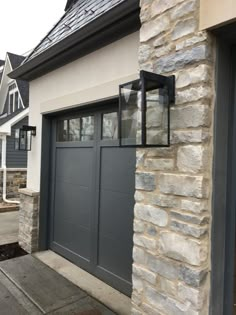 a gray garage door with two windows on the side of it and stone pillars in front