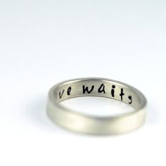 a silver ring with the word we wait on it's side and an inscription in black ink