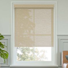 a living room with a couch, chair and large window covered in beige roman shades