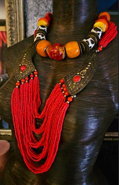 Here's a Bohemian Necklace and Bib Set I found in my inventory. The longer strand is a vintage piece that I did not make. It measures a non-adjustable 28" and closes with a button and a loop. Multiple strands of red-orange seed beads comprise the majority of the piece and two ornate metal accents (looks like bronze) are symmetrically set on each side with an orange-red cabochon (jade??). The shorter necklace is one that I made. It measures a non-adjustable 19" and features the following components: Tibetan resin, Moroccan resin, Zebu bone*, gold tone metal spacers, vintage Chinese brass coins, red branch corals, vintage brass beads and round tiger's eye. Closes with a gold tone hook and eye. Pair them together, or wear separately. These also will mix and match well with your personal favor Adjustable Necklace With Large Beads For Rituals, Adjustable Beaded Necklaces For Rituals, Vintage Red Hand-strung Beaded Necklaces, Multi-strand Dangling Beads Festival Jewelry, Artisan Beaded Necklaces For Rituals, Festival Multi-strand Dangling Beads Jewelry, Festival Multi-strand Jewelry With Dangling Beads, Unique Dangling Beads For Festivals, Artisan Style Beaded Chain Necklace