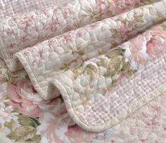 a pink and white floral quilted bed spread on top of a tablecloth with flowers