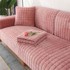 a pink velvet couch with matching pillows and blankets on it in front of a plant