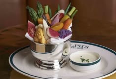 a silver cup filled with assorted veggies on top of a white plate