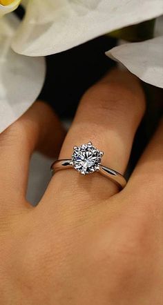 a woman's hand with a diamond ring on it and flowers in the background