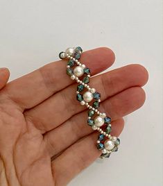 a hand holding a beaded bracelet with pearls and blue glass beads on the end