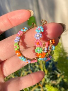 Handmade beaded hoop earrings 3.5 cm in diameter. The daisies are blue, pink, purple, green, and orange; perfect for spring or summer. They are lightweight, and the beads are mounted on a gold colored stainless steel hoop with a latch back closure. Beaded Earrings Hoop, Rainbow Bohemian Jewelry For Spring, Spring Jewelry With Colorful Beads In Gold, Bohemian Rainbow Jewelry For Spring, Spring Gold Jewelry With Colorful Beads, Spring Rainbow Bohemian Jewelry, Bohemian Dangle Hoop Earrings For Spring, Trendy Flower Hoop Earrings For Summer, Handmade Multicolor Flower Earrings For Spring