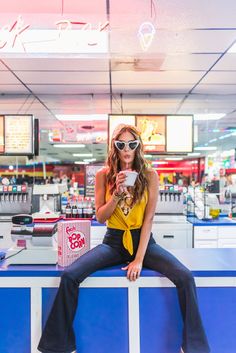 a woman sitting on top of a blue counter holding a cup in her right hand