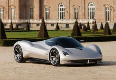 a silver sports car parked in front of a large building with trees and bushes around it