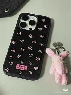 a pink teddy bear keychain sitting next to an iphone case