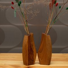 two wooden vases with dried flowers in them on a wood table next to a wall