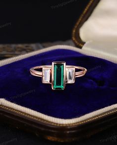 an emerald and diamond ring sitting on top of a velvet case