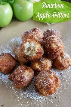 some sugar covered doughnuts sitting on top of a table next to green apples