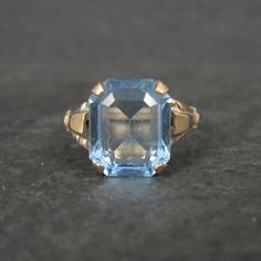 This gorgeous vintage ring is 10K Gold Filled. It features a stunning 10x12mm faceted blue glass stone. The face of this ring measures 1/2 of an inch north to south with a rise of 7mm off the finger. Size: 9 Marks: 1/20 10K GF, MH Condition: Old new stock - excellent Vintage Blue Topaz Ring With Diamond Cut, Vintage Sapphire Topaz Promise Ring, Vintage Blue Topaz Ring In 14k Gold, Vintage Blue Gemstone Birthstone Ring, Vintage Octagon Jewelry Gift, Vintage Octagon Diamond Cut Jewelry, Antique Blue Topaz Ring Hallmarked, Vintage Faceted Rings For Anniversary, Classic Blue Octagon Topaz Ring