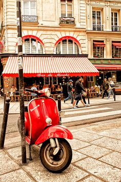 a red scooter parked on the side of a street next to a tall building