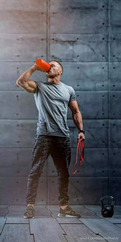 a man drinking from a red cup while standing in front of a gray wall with his hands behind his head