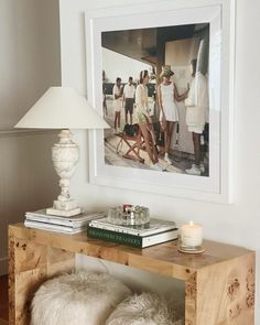 a wooden table topped with books and a lamp next to a framed photograph on the wall