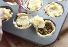 a person scooping mashed potatoes into a muffin tin filled with meat and veggies