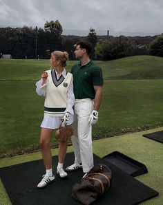 a man standing next to a woman on top of a green golf course in the rain