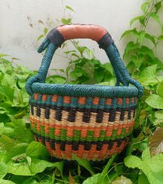 a woven basket sitting in the middle of some green plants and grass with leaves around it