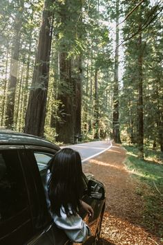 a woman sitting in the passenger seat of a car next to a tree lined road