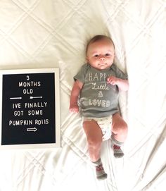 a baby laying on top of a bed next to a sign