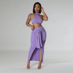 a woman wearing a purple skirt and crop top with high slits, standing in front of a white background