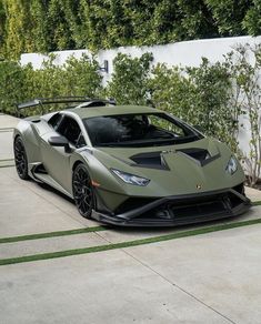 a green sports car parked in front of a white wall and some bushes next to it