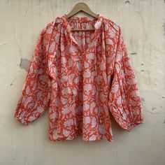 This divine cotton blouse is as light as can be. With the most romantic billowed sleeves, elastic cuffs, and two optional ties at the front. The flowing fabric features a sweet floral classic Indian Buti block print in cinnamon on soft white cotton. A timeless feminine piece. Material ~ 100% Cotton. Depending on each individual, some find the material sheer.  Garment Care ~ We recommend a gentle, cold water hand wash using natural detergents, and hang drying in the shade. Handcrafted garments ar Orange Long Sleeve Blouse With Relaxed Fit, Orange Relaxed Fit Long Sleeve Blouse, Summer Printed Tops With Lantern Sleeves, Summer Lantern Sleeve Printed Tops, Summer Tops With Gathered Sleeves And Flowy Fit, Summer Tops With Gathered Sleeves, Flowy Fit, Summer Flowy Top With Gathered Sleeves, Orange Cotton Blouse For Summer, Bohemian Flowy Top With Puff Sleeves