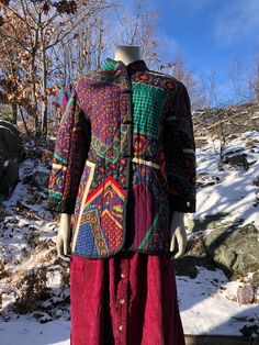 a mannequin wearing a colorful jacket and skirt in front of snow covered ground