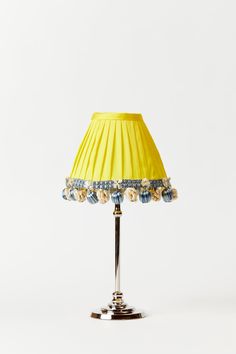 a lamp that is on top of a metal stand with a yellow shade over it